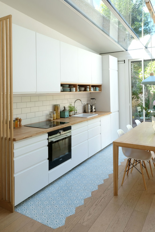 Idéer för mellanstora skandinaviska linjära kök med öppen planlösning, med en undermonterad diskho, släta luckor, vita skåp, träbänkskiva, vitt stänkskydd, stänkskydd i keramik, integrerade vitvaror, cementgolv och blått golv