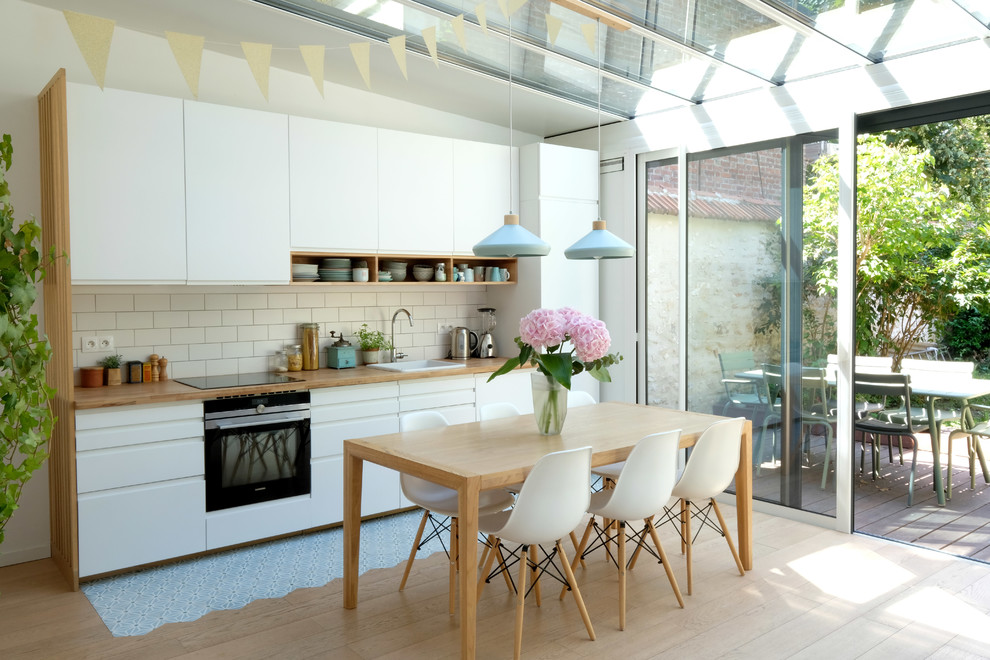 Photo of a medium sized scandinavian single-wall kitchen/diner in Paris with flat-panel cabinets, white cabinets, wood worktops, white splashback, ceramic splashback, integrated appliances, cement flooring, no island, a built-in sink and blue floors.