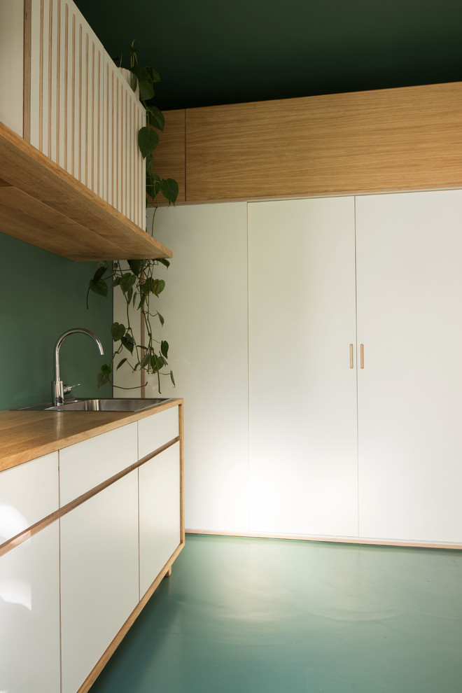 Modelo de cocinas en L contemporánea de tamaño medio abierta con fregadero de un seno, puertas de armario blancas, encimera de madera, salpicadero gris, electrodomésticos con paneles y suelo de cemento