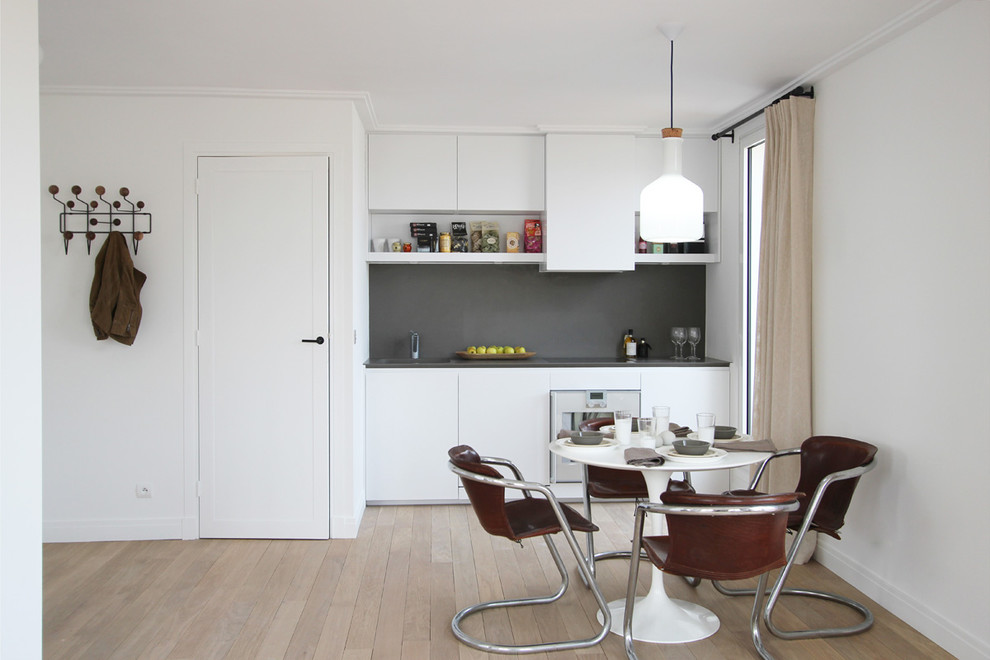 Пример оригинального дизайна: маленькая прямая, серо-белая кухня в стиле модернизм с обеденным столом, плоскими фасадами, белыми фасадами и серым фартуком без острова для на участке и в саду