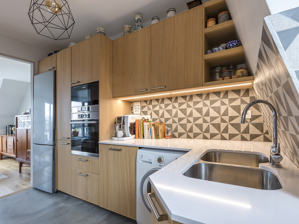 Cette image montre une cuisine design en L et bois clair de taille moyenne avec un évier encastré, un placard à porte plane, une crédence multicolore, un sol gris et un plan de travail blanc.