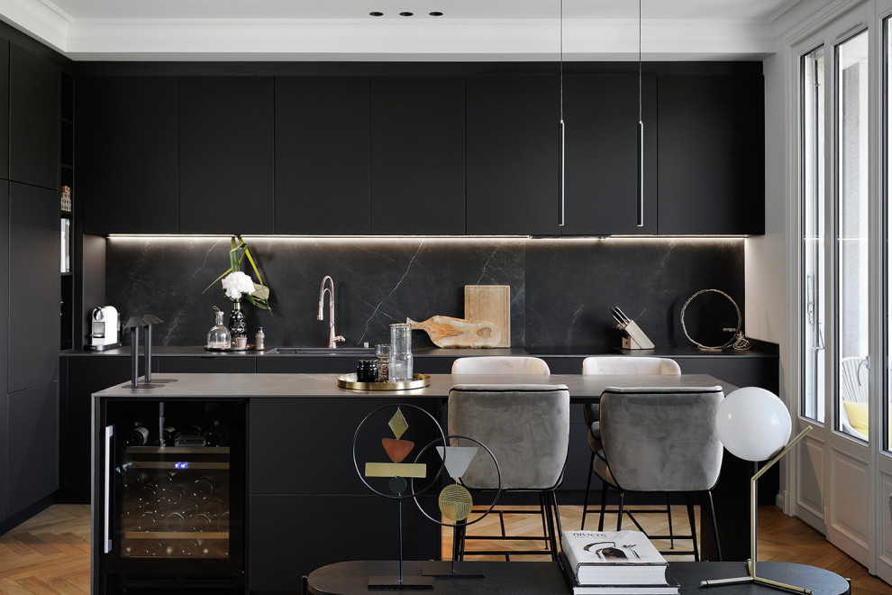 Offene Moderne Küche mit flächenbündigen Schrankfronten, schwarzen Schränken, Küchenrückwand in Schwarz, Rückwand aus Stein, hellem Holzboden, Kücheninsel und grauer Arbeitsplatte in Lyon