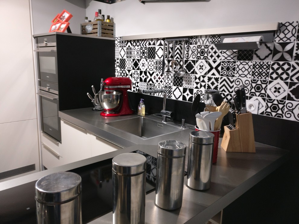 Esempio di una piccola cucina contemporanea con lavello sottopiano, ante a filo, ante bianche, top in acciaio inossidabile, paraspruzzi nero, paraspruzzi con piastrelle di cemento, elettrodomestici in acciaio inossidabile, pavimento in laminato e pavimento nero