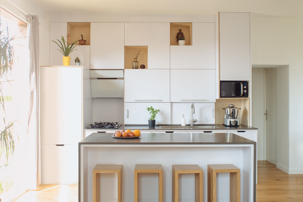 Design ideas for a medium sized contemporary galley kitchen in Bordeaux with a built-in sink, flat-panel cabinets, white cabinets, integrated appliances, light hardwood flooring, an island, beige floors and grey worktops.
