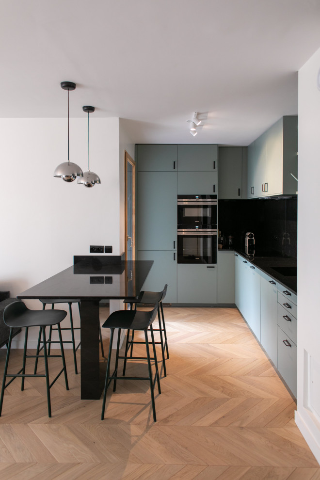 Inspiration for a small modern l-shaped open plan kitchen in Le Havre with a submerged sink, beaded cabinets, green cabinets, marble worktops, black splashback, marble splashback, stainless steel appliances, light hardwood flooring, an island and black worktops.