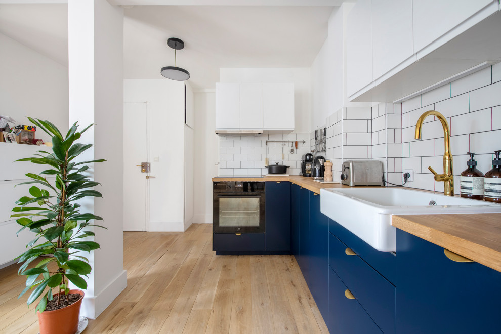 This is an example of a medium sized scandinavian single-wall open plan kitchen in Paris with a single-bowl sink, flat-panel cabinets, blue cabinets, wood worktops, white splashback, cement tile splashback, coloured appliances, light hardwood flooring, multiple islands, beige floors and beige worktops.