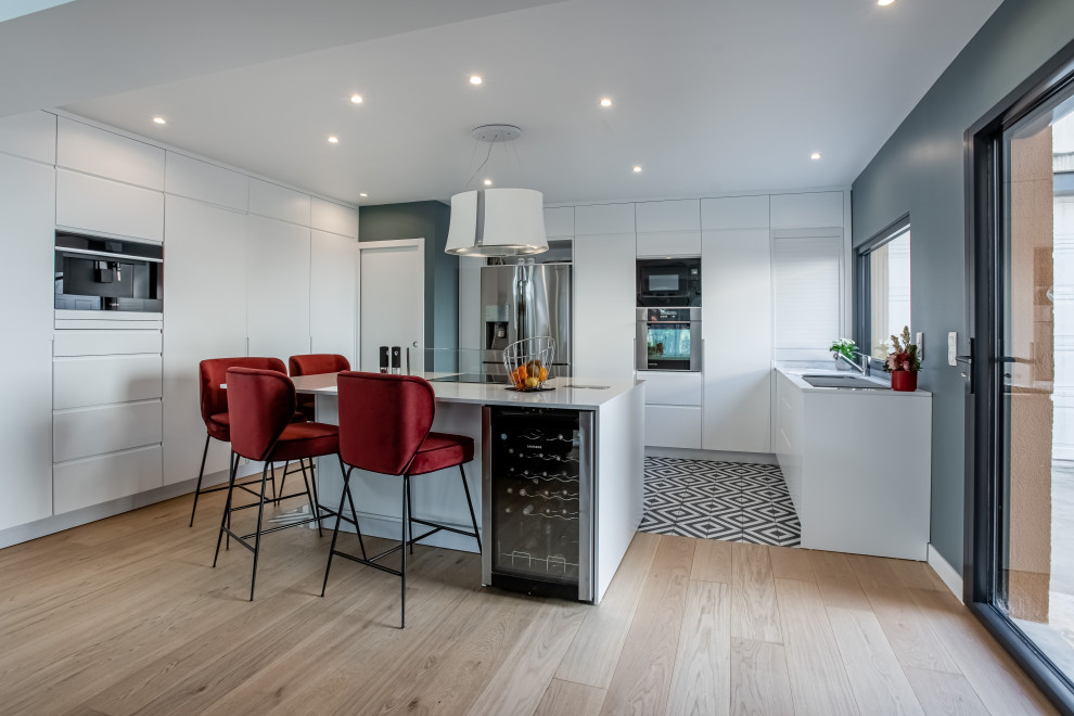 Kitchen - mid-sized contemporary u-shaped porcelain tile and multicolored floor kitchen idea in Paris with flat-panel cabinets, white cabinets, mirror backsplash, paneled appliances, an island and white countertops
