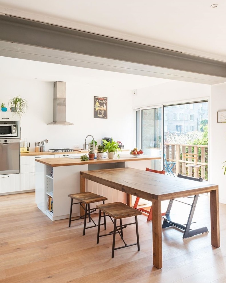 Exempel på ett stort modernt brun brunt kök, med en nedsänkt diskho, vita skåp, träbänkskiva, rostfria vitvaror, ljust trägolv, en köksö, släta luckor, vitt stänkskydd och brunt golv