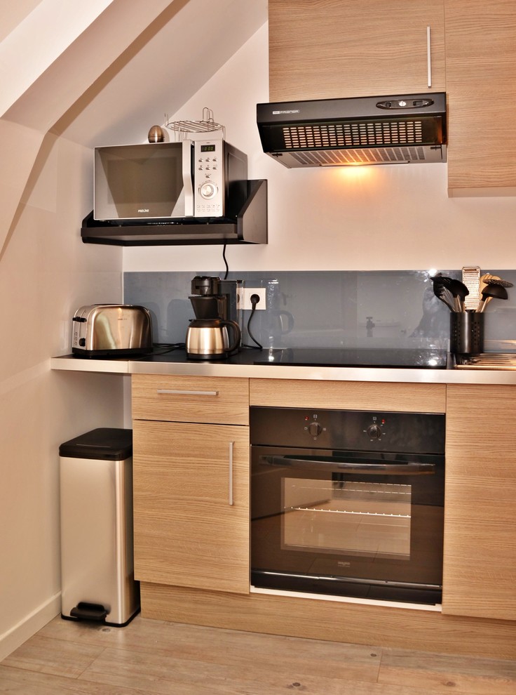 Exempel på ett litet modernt grå linjärt grått kök, med en nedsänkt diskho, släta luckor, skåp i ljust trä, laminatbänkskiva, grått stänkskydd, glaspanel som stänkskydd, svarta vitvaror, ljust trägolv och beiget golv