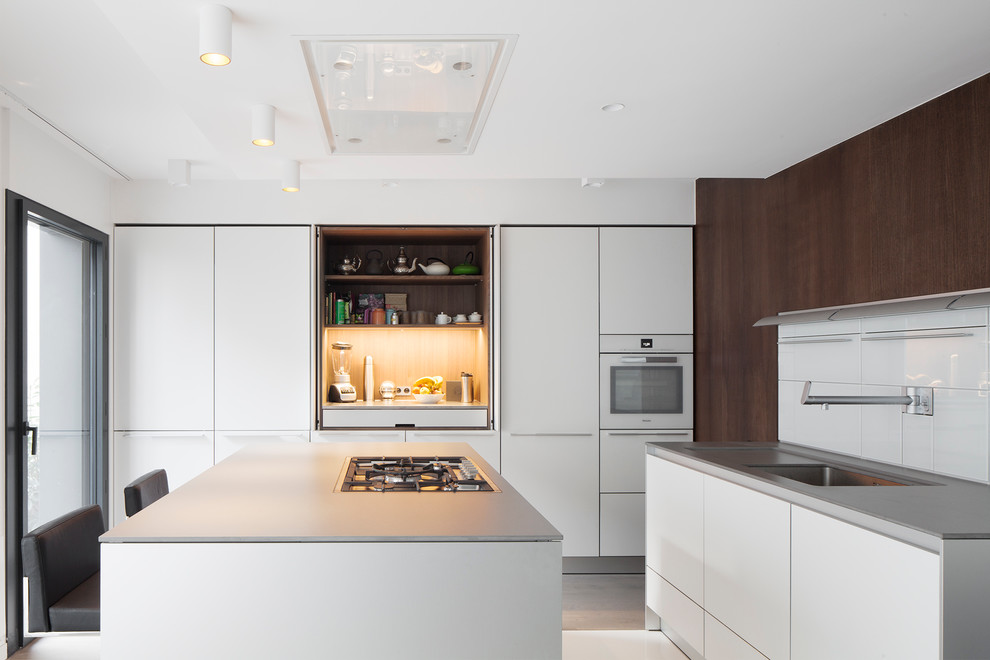 Modelo de cocina comedor contemporánea grande con puertas de armario blancas, salpicadero blanco, una isla, fregadero bajoencimera, armarios con paneles lisos y electrodomésticos blancos