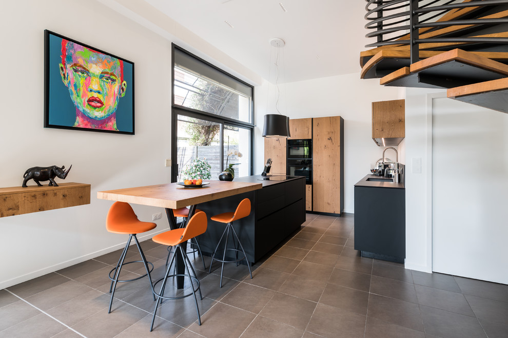Contemporary l-shaped kitchen in Lyon with a submerged sink, flat-panel cabinets, medium wood cabinets, black appliances, an island, grey floors and black worktops.