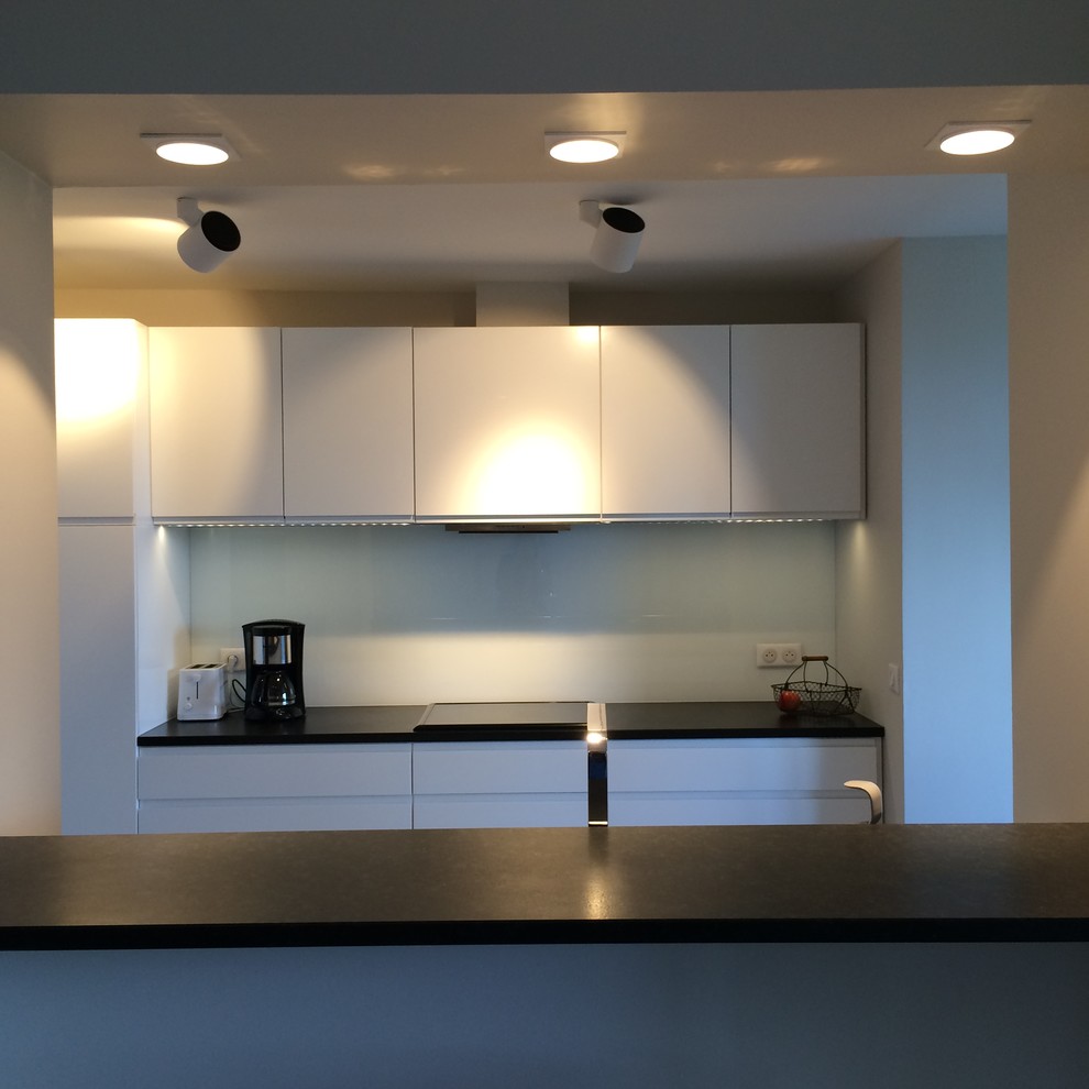 Foto di una cucina design di medie dimensioni con lavello sottopiano, ante a filo, ante bianche, top in granito, paraspruzzi bianco, paraspruzzi con lastra di vetro, elettrodomestici in acciaio inossidabile, pavimento con piastrelle in ceramica e pavimento grigio