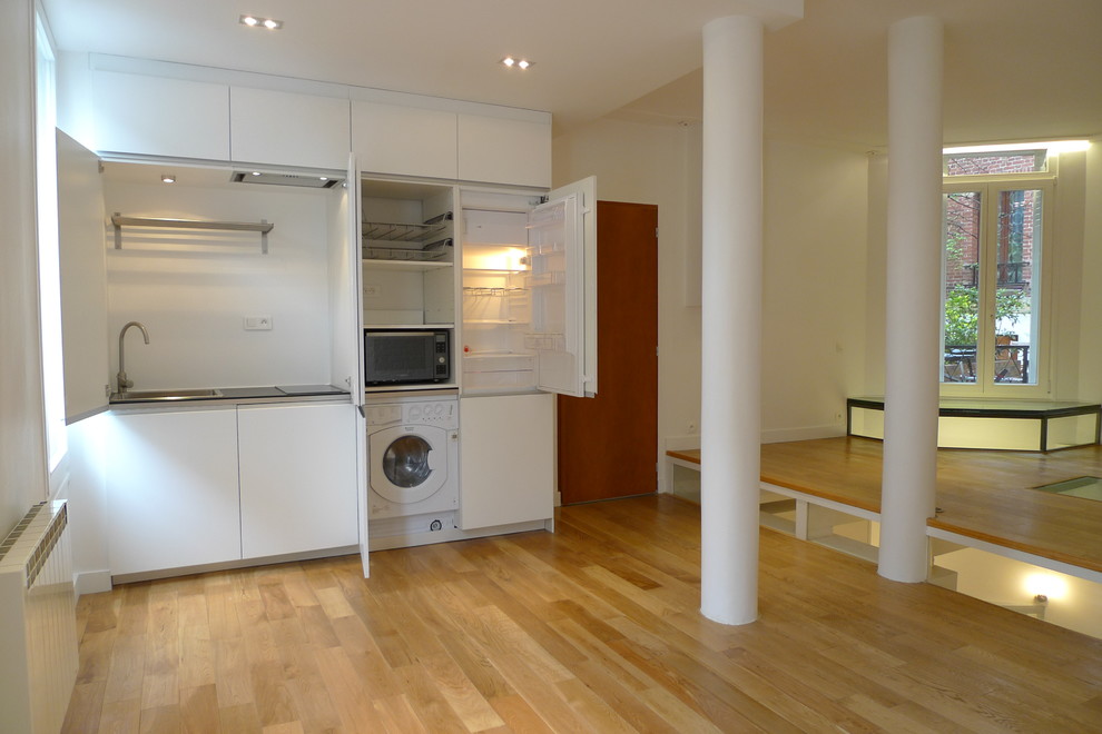 Exempel på ett litet modernt linjärt kök med öppen planlösning, med en undermonterad diskho, luckor med profilerade fronter, vita skåp, laminatbänkskiva, vitt stänkskydd, vita vitvaror, ljust trägolv och beiget golv