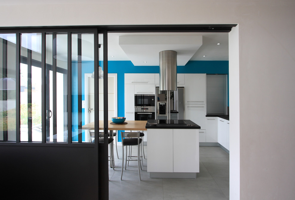 This is an example of a medium sized modern l-shaped kitchen/diner in Angers with an integrated sink, flat-panel cabinets, white cabinets, granite worktops, black splashback, glass sheet splashback, stainless steel appliances and an island.