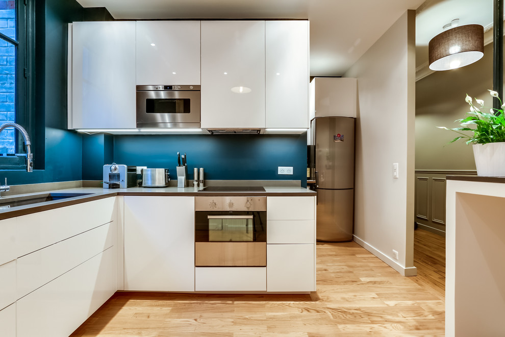 Moderne Küche ohne Insel in L-Form mit Unterbauwaschbecken, flächenbündigen Schrankfronten, weißen Schränken, Küchengeräten aus Edelstahl und hellem Holzboden in Paris