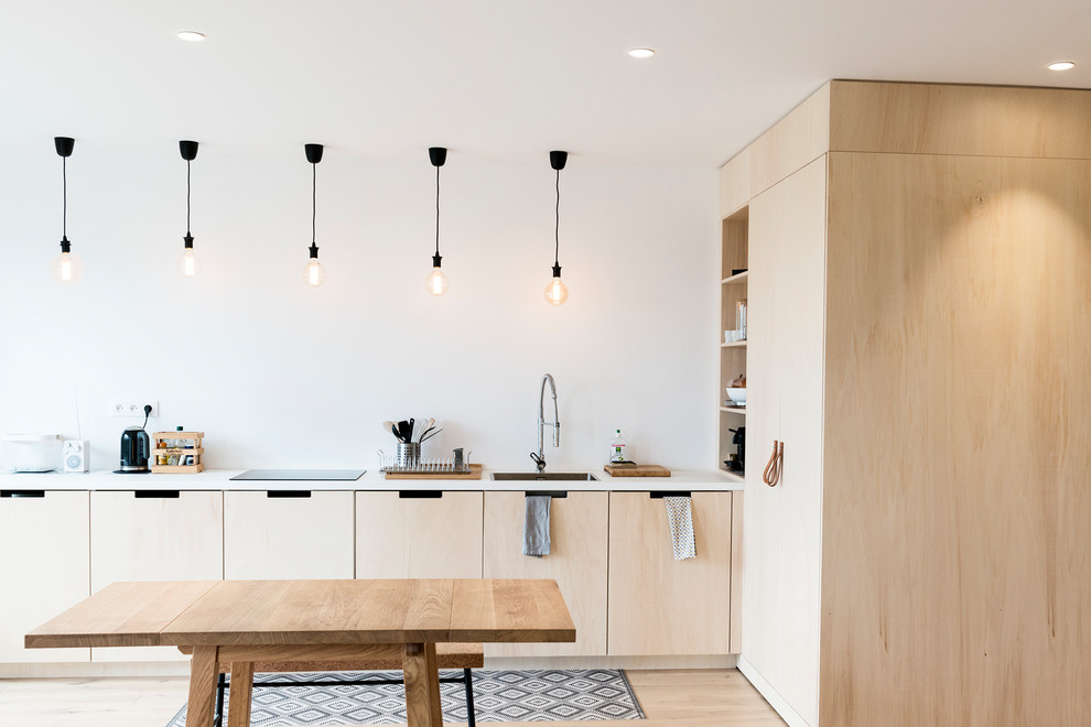 На фото: кухня в скандинавском стиле с обеденным столом, одинарной мойкой, плоскими фасадами, светлыми деревянными фасадами, светлым паркетным полом и белой столешницей