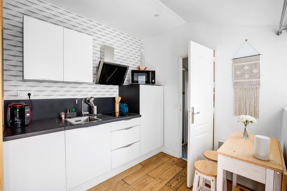 Idéer för att renovera ett litet skandinaviskt svart linjärt svart kök och matrum, med vita skåp, laminatbänkskiva, svart stänkskydd, en nedsänkt diskho, släta luckor, mellanmörkt trägolv och brunt golv