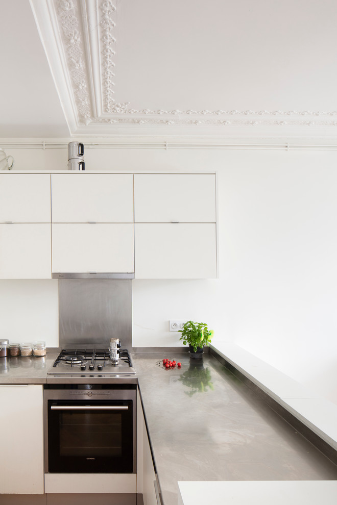 This is an example of a medium sized contemporary l-shaped open plan kitchen in Paris with white cabinets, stainless steel worktops, white splashback and grey worktops.
