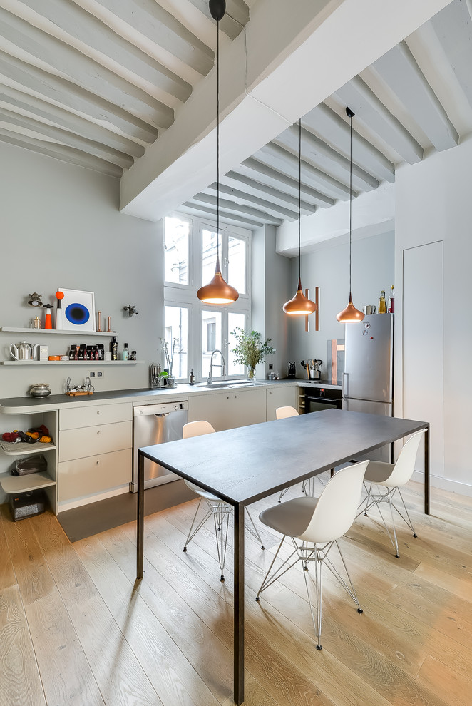 На фото: угловая кухня среднего размера в скандинавском стиле с плоскими фасадами, белыми фасадами, техникой из нержавеющей стали, светлым паркетным полом и обеденным столом