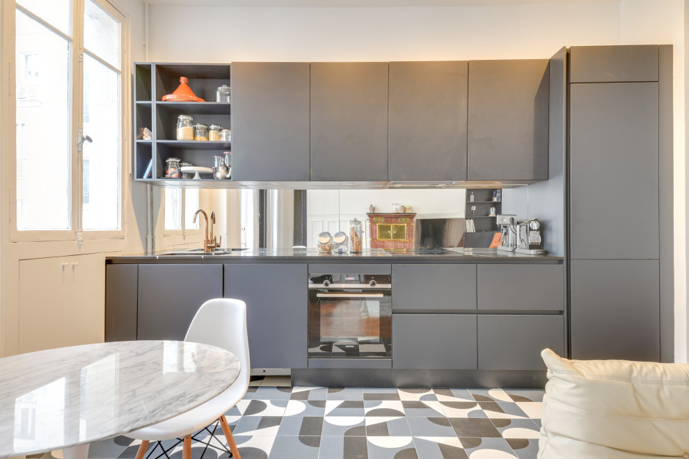 Foto på ett skandinaviskt linjärt kök med öppen planlösning, med en enkel diskho, släta luckor, grå skåp, bänkskiva i rostfritt stål, spegel som stänkskydd och flerfärgat golv