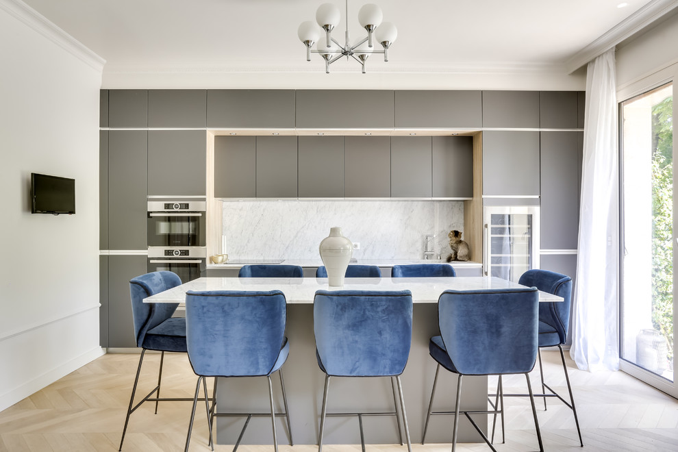 Large contemporary single-wall kitchen/diner in Paris with grey cabinets, marble worktops, white splashback, marble splashback, stainless steel appliances, light hardwood flooring, an island, white worktops, a submerged sink, beaded cabinets and brown floors.