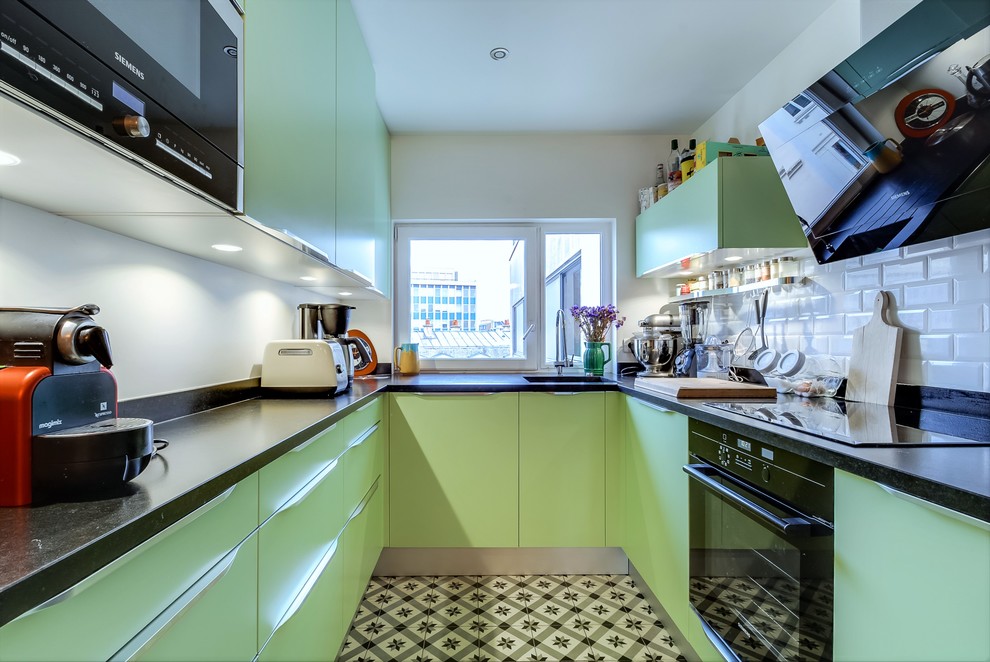 This is an example of a medium sized contemporary u-shaped enclosed kitchen in Paris with flat-panel cabinets, green cabinets, granite worktops, white splashback, metro tiled splashback, black appliances, ceramic flooring and no island.