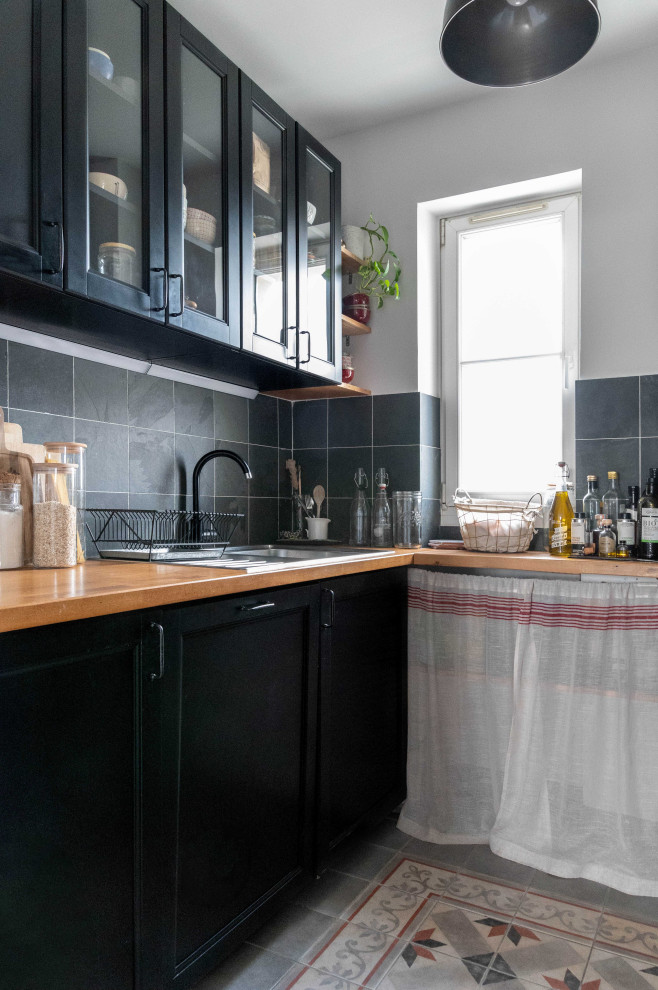 パリにある小さなミッドセンチュリースタイルのおしゃれなキッチン (アンダーカウンターシンク、黒いキャビネット、木材カウンター、グレーのキッチンパネル、スレートのキッチンパネル、黒い調理設備、セメントタイルの床、グレーの床) の写真