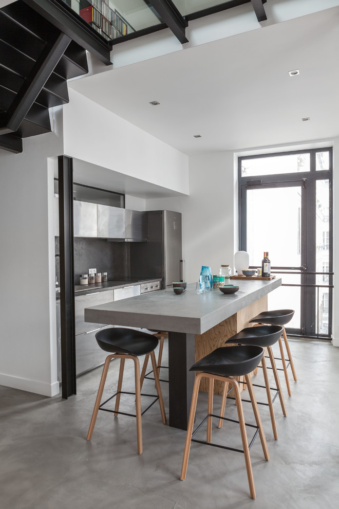Cette image montre une cuisine ouverte parallèle design en inox de taille moyenne avec un placard à porte plane, une crédence grise, sol en béton ciré et îlot.