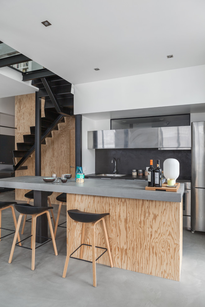 Imagen de cocina lineal actual pequeña abierta con fregadero bajoencimera, salpicadero negro, electrodomésticos de acero inoxidable, suelo de cemento y una isla