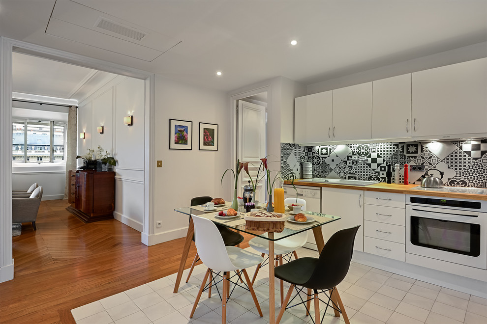 Example of a large trendy l-shaped ceramic tile open concept kitchen design in Paris with beaded inset cabinets, white cabinets, wood countertops, cement tile backsplash, white appliances, a drop-in sink and multicolored backsplash