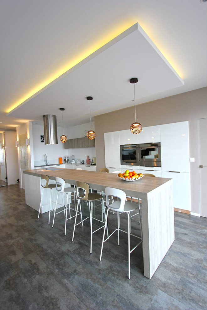 This is an example of a medium sized contemporary u-shaped kitchen/diner in Lyon with a submerged sink, white cabinets, laminate countertops, white splashback, stainless steel appliances, laminate floors, an island, beige worktops, flat-panel cabinets, glass sheet splashback and grey floors.