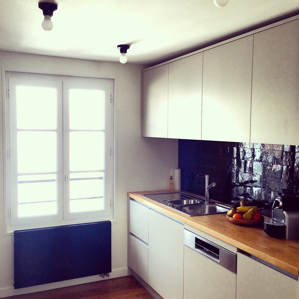 На фото: параллельная кухня-гостиная среднего размера в современном стиле с плоскими фасадами, деревянной столешницей и серыми фасадами