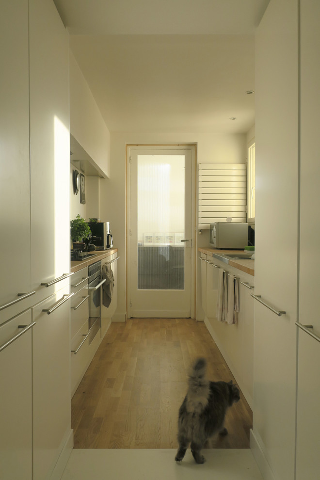 Immagine di una cucina minimal di medie dimensioni con ante a filo, ante bianche, top in legno, paraspruzzi bianco, pavimento in laminato e nessuna isola