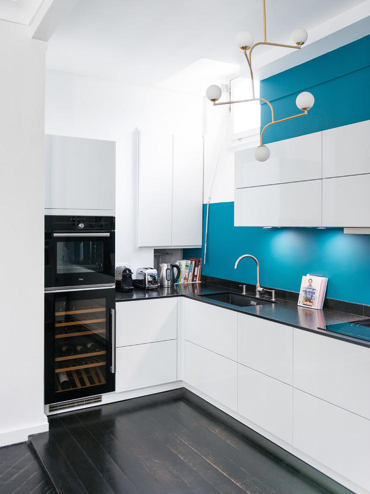 Exemple d'une cuisine ouverte tendance en L de taille moyenne avec un évier intégré, des portes de placard blanches, un plan de travail en granite, une crédence bleue, un électroménager noir, parquet peint et un sol noir.