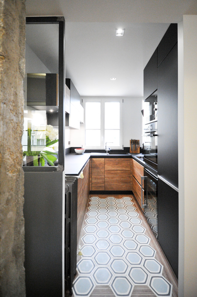 Cette image montre une cuisine bicolore design en U avec un placard à porte plane, des portes de placard noires, une péninsule et un sol bleu.