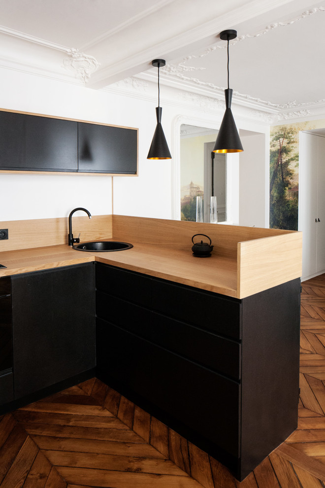 Modern inredning av ett mellanstort kök, med en undermonterad diskho, släta luckor, svarta skåp, träbänkskiva, beige stänkskydd, stänkskydd i trä, mellanmörkt trägolv och brunt golv