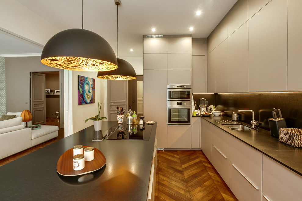 Design ideas for a large modern l-shaped kitchen/diner in Paris with a submerged sink, beaded cabinets, grey cabinets, granite worktops, black splashback, marble splashback, stainless steel appliances, medium hardwood flooring, an island and brown floors.