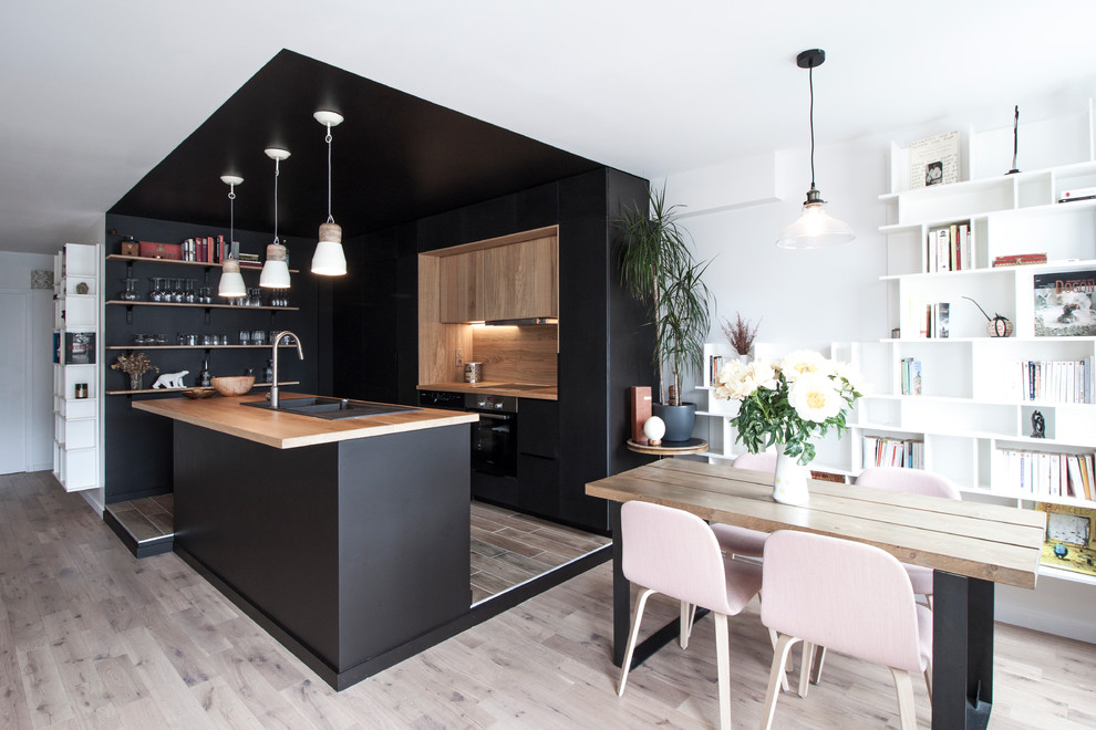 Пример оригинального дизайна: параллельная кухня-гостиная среднего размера в скандинавском стиле с двойной мойкой, деревянной столешницей, черной техникой, светлым паркетным полом, островом, коричневым фартуком, черно-белыми фасадами и двухцветным гарнитуром