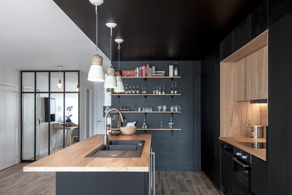 На фото: параллельная кухня-гостиная среднего размера в скандинавском стиле с двойной мойкой, черными фасадами, деревянной столешницей, черной техникой, островом, коричневым фартуком и полом из керамической плитки