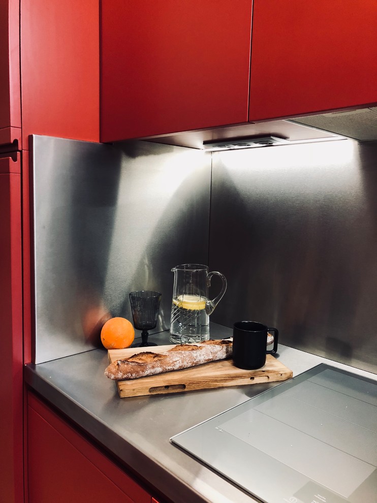 パリにある高級なトランジショナルスタイルのおしゃれなキッチン (一体型シンク、インセット扉のキャビネット、赤いキャビネット、ステンレスカウンター、グレーのキッチンパネル、パネルと同色の調理設備、淡色無垢フローリング、茶色い床、グレーのキッチンカウンター) の写真