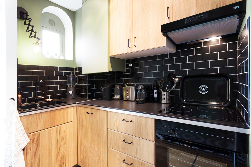 Foto på ett litet funkis kök, med en enkel diskho, luckor med profilerade fronter, skåp i ljust trä, laminatbänkskiva, svart stänkskydd, stänkskydd i tunnelbanekakel och svarta vitvaror