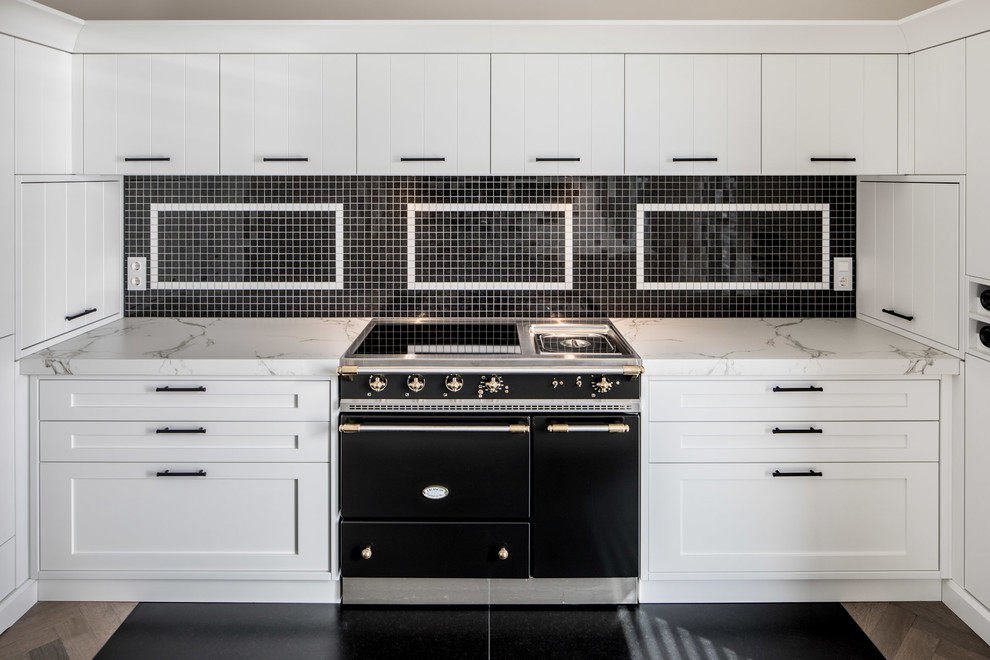 Пример оригинального дизайна: кухня в современном стиле с разноцветным фартуком, фартуком из плитки мозаики, черной техникой, разноцветным полом, белой столешницей и черно-белыми фасадами