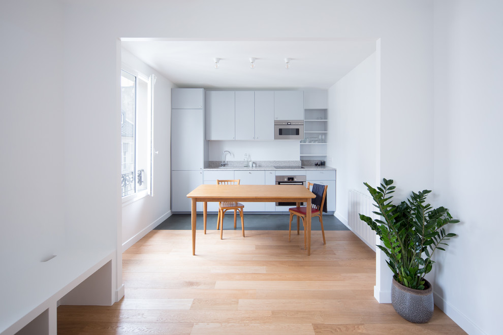 Idéer för små funkis linjära grått kök med öppen planlösning, med en undermonterad diskho, luckor med profilerade fronter, vita skåp, granitbänkskiva, grått stänkskydd, rostfria vitvaror, ljust trägolv och brunt golv