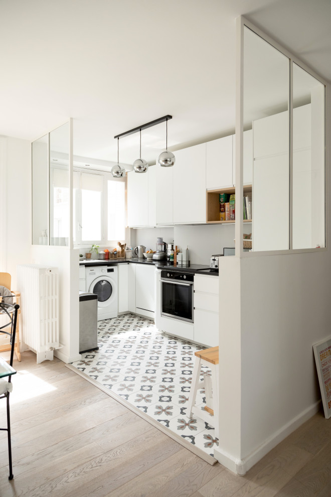 Medium sized modern l-shaped open plan kitchen in Other with a built-in sink, flat-panel cabinets, white cabinets, granite worktops, grey splashback, stainless steel appliances, cement flooring, no island, multi-coloured floors and black worktops.