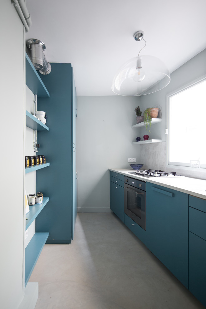 Zweizeilige Moderne Küche ohne Insel mit flächenbündigen Schrankfronten, blauen Schränken, schwarzen Elektrogeräten, beigem Boden, weißer Arbeitsplatte, Küchenrückwand in Blau und Betonboden in Paris
