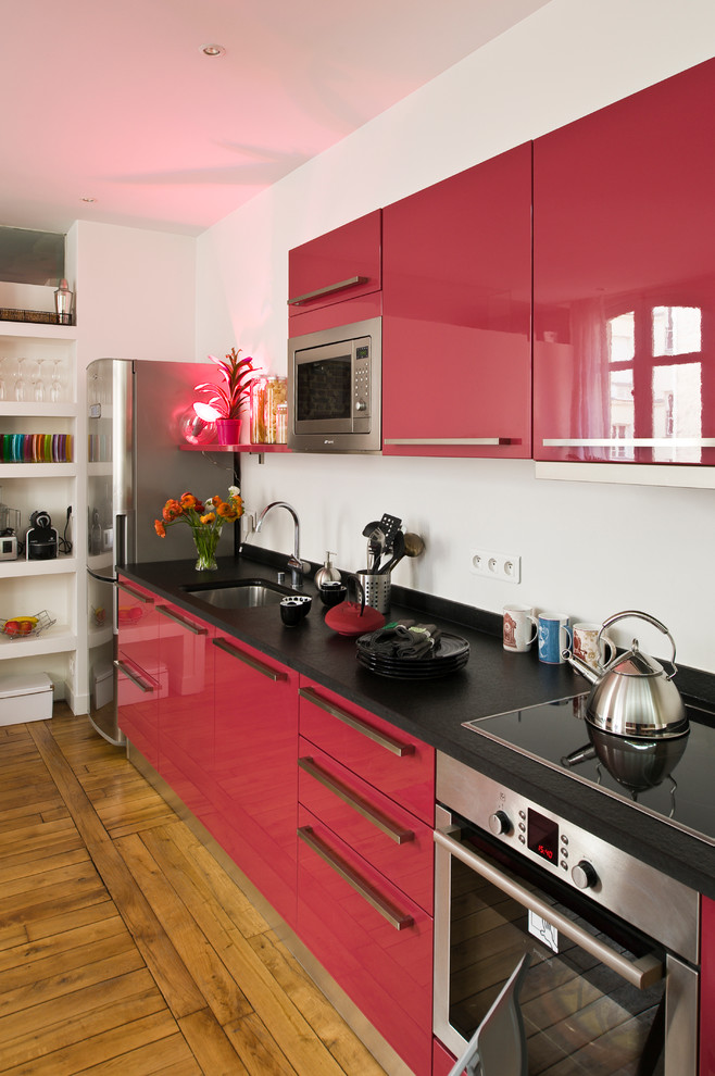 Foto de cocina lineal y estrecha contemporánea de tamaño medio abierta sin isla con puertas de armario rojas y suelo de madera en tonos medios