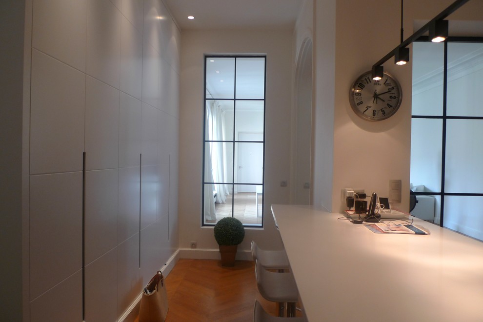 Diseño de cocina lineal contemporánea pequeña cerrada con puertas de armario blancas, una isla, suelo marrón, encimeras blancas, armarios con paneles lisos y suelo de madera clara