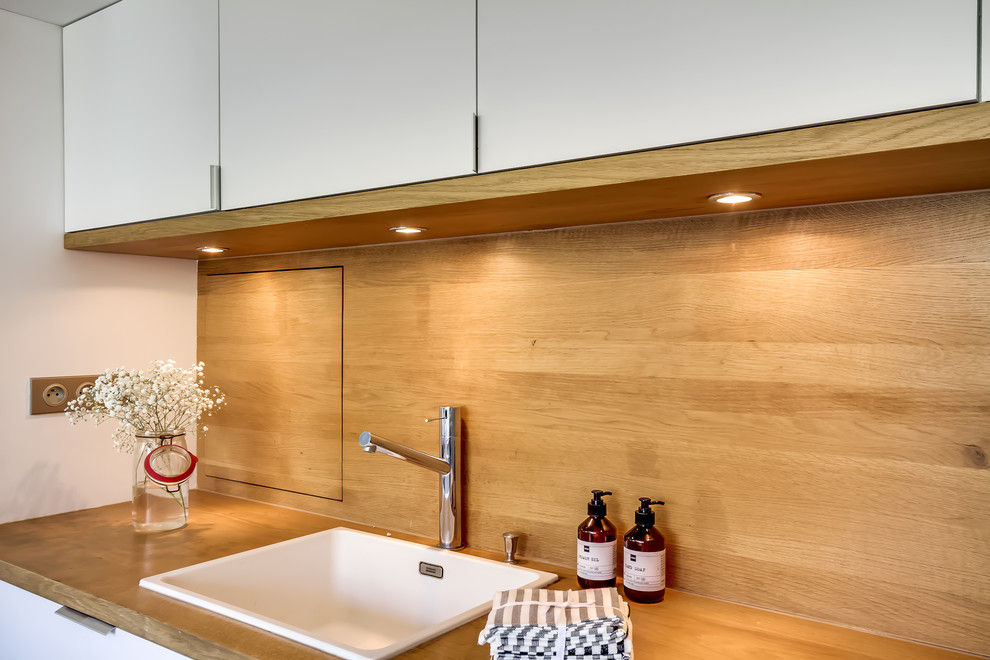 Idéer för mellanstora minimalistiska linjära beige kök och matrum, med en enkel diskho, släta luckor, vita skåp, träbänkskiva, beige stänkskydd, stänkskydd i trä, integrerade vitvaror, mellanmörkt trägolv, en köksö och brunt golv