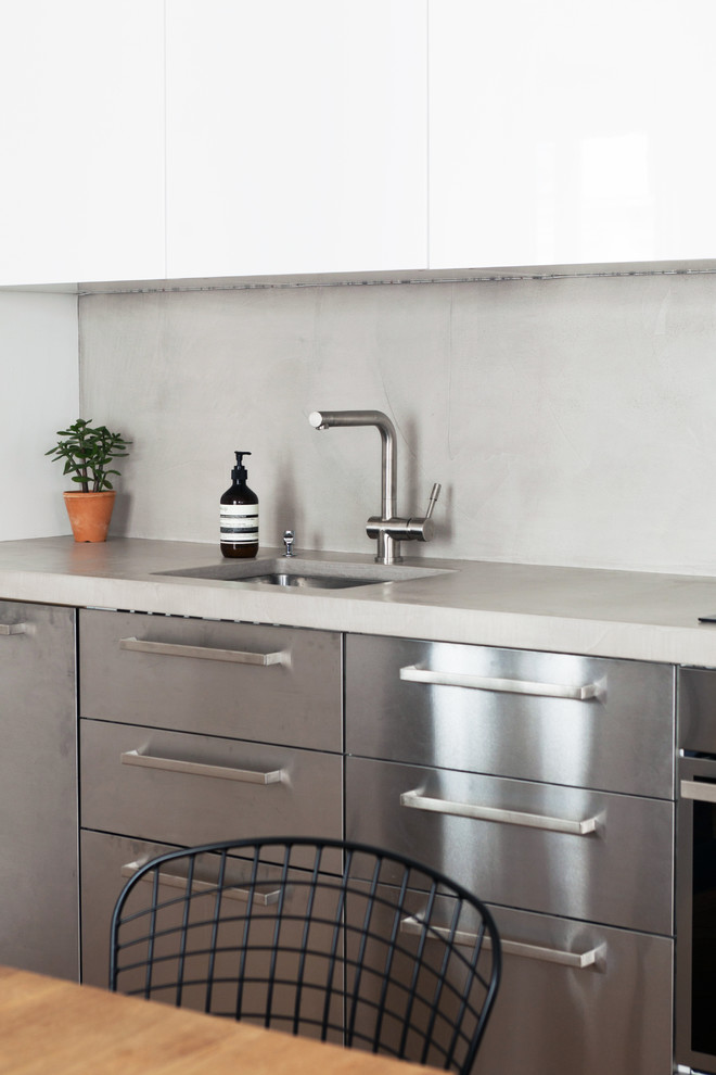 Modern inredning av ett mellanstort grå linjärt grått kök med öppen planlösning, med en undermonterad diskho, släta luckor, skåp i rostfritt stål, bänkskiva i betong, grått stänkskydd, integrerade vitvaror, mellanmörkt trägolv och brunt golv