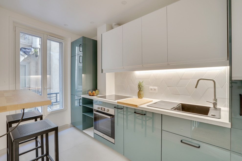 Exempel på ett avskilt, mellanstort modernt vit linjärt vitt kök, med en nedsänkt diskho, släta luckor, blå skåp, vitt stänkskydd, integrerade vitvaror, laminatbänkskiva, stänkskydd i keramik, cementgolv och grått golv